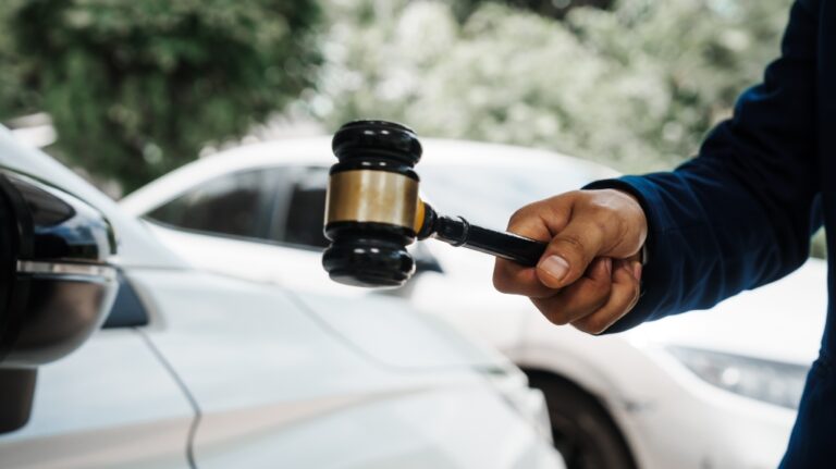 lawyer holding a wooden gavel stands in front of a car