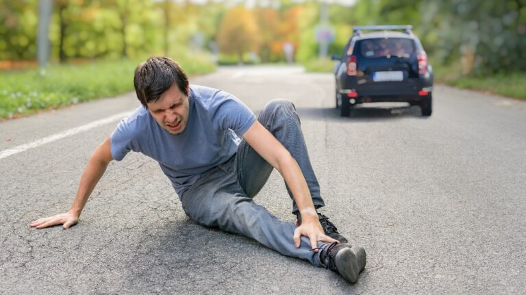 Injured man on road in front of a car