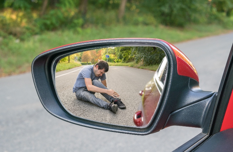 View on injured man on road in rear mirror of a car