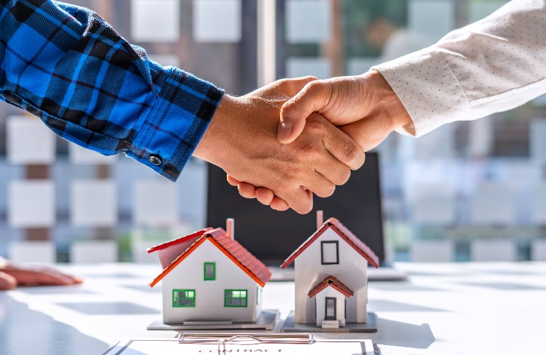 Men shake hands in front of two model houses