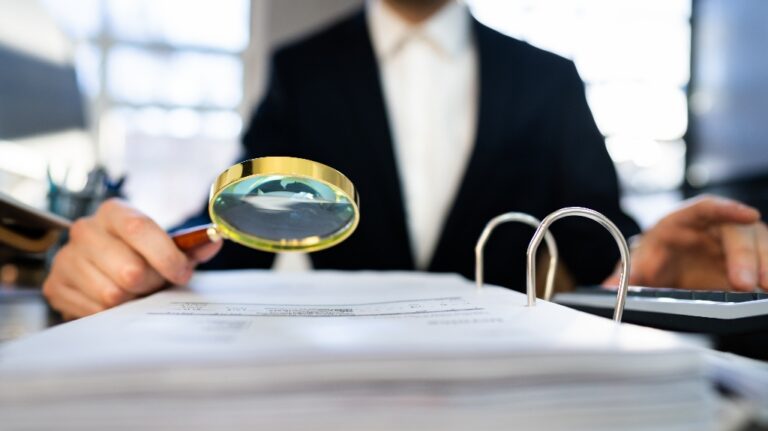 man looks at documents through a magnifying glass