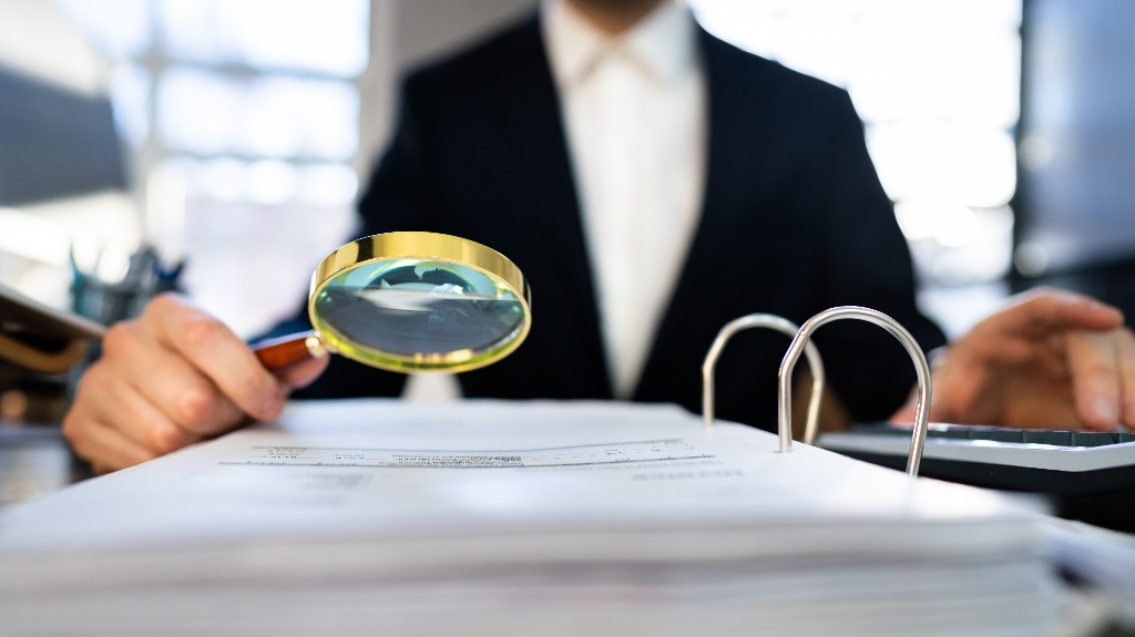 man looks at documents through a magnifying glass