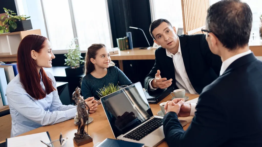 Four people, including a woman and child, engaged in a professional office discussion around a table.